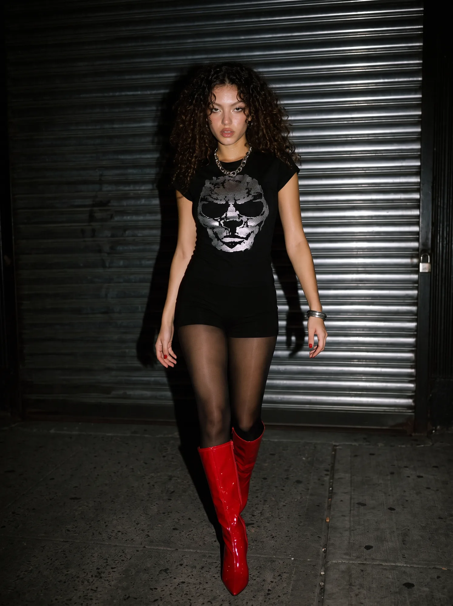Model in a skull T-shirt and red patent boots against a metal shutter