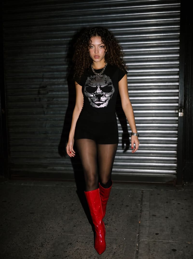 Model in a skull T-shirt and red patent boots against a metal shutter